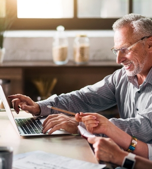 Imagen de una pareja de ancianos sentada en la cocina, usando la computadora y sonriendo