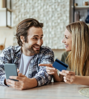 Imagen de un hombre alegre de haber sorprendido a la familia milenaria europea con teléfono y tarjeta de crédito, esposa rubia señalando con el dedo el gadget