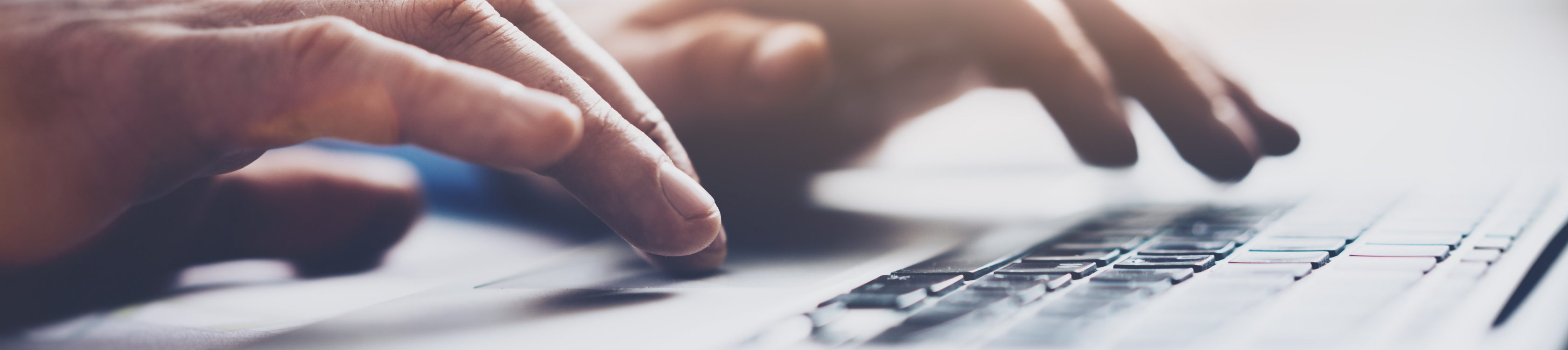 Hände tippen auf Laptop, der auf weißem Schreibtisch steht.