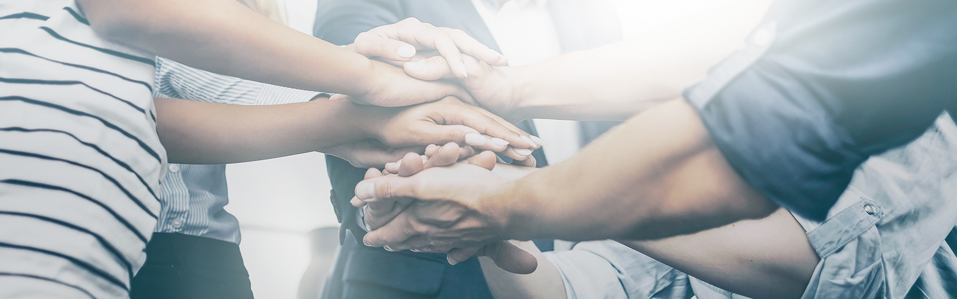 Eine Menschengruppe steht im Kreis und legen ihre Hände in der Mitte aufeinander.