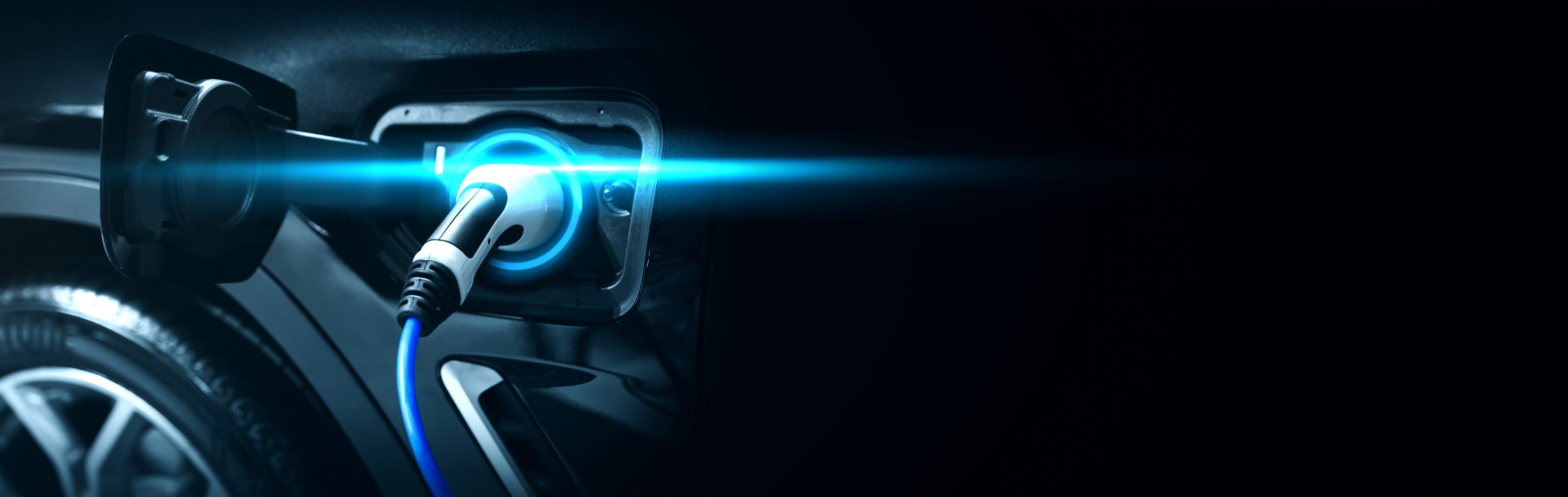 Links ist der Reifen sowie das Ladegerät eines E-Autos zu sehen. Das Gerät leuchtet blau, um die Spannung zu symbolisieren.