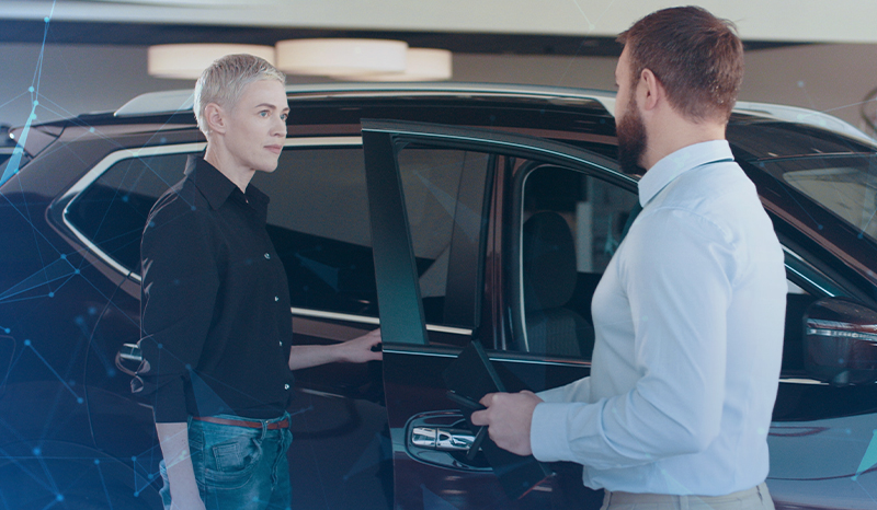 Zwei Personen stehen vor einem schwarzen Auto, dessen Beifahrertür geöffnet ist.