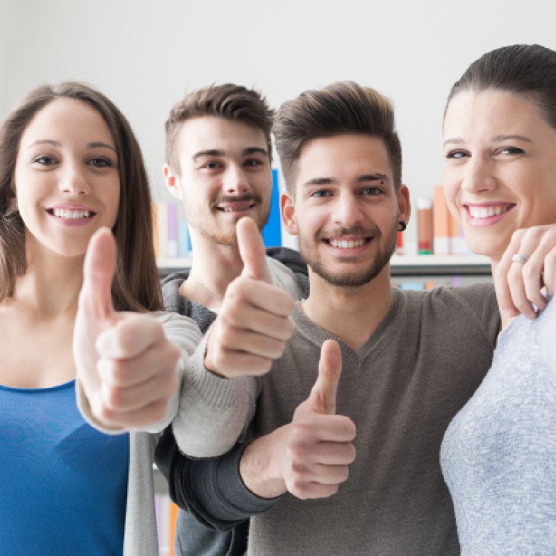 Four students smiling doing the thumbs up hand gesture.