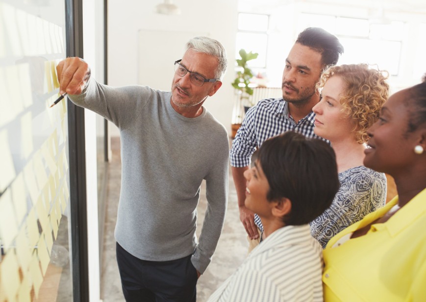 Groupe de 5 personnes réuni autour d'un tableau avec des post-it