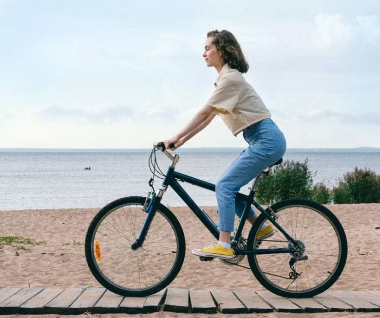 Junge Frau auf Fahrrad, die Küste zuversichtlich entlang fahrend