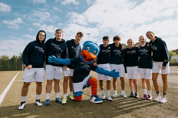 Eine Gruppe junger Sportler posiert glücklich mit einem blauen Vogel-Maskottchen