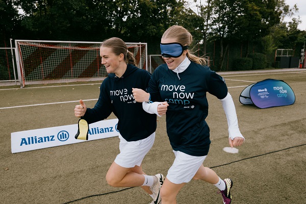 Zwei Sportlerinnen laufen zusammen, eine mit verbundenen Augen, während des MoveNow-Camps 