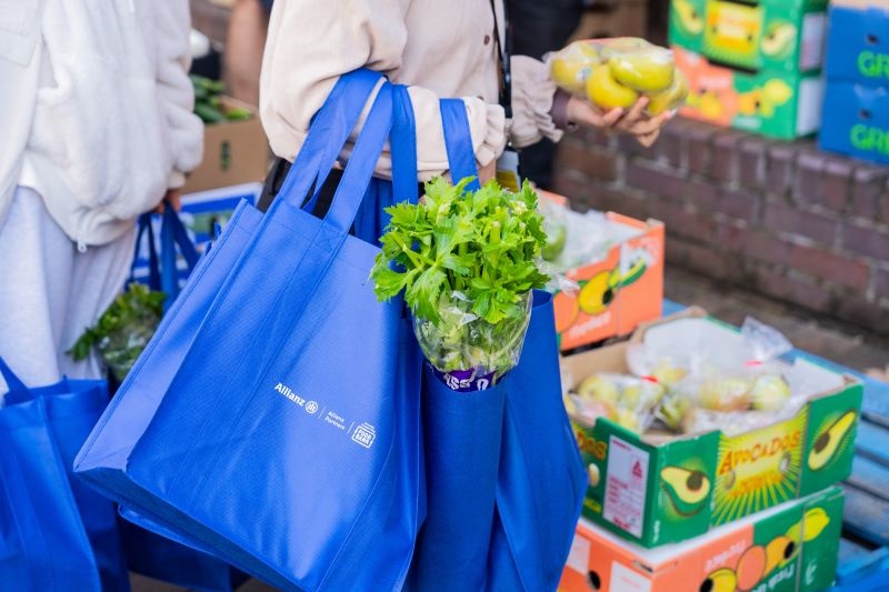 Blue Allianz Partner Foodbank bag, with the green leaves of celery sticks poking out.