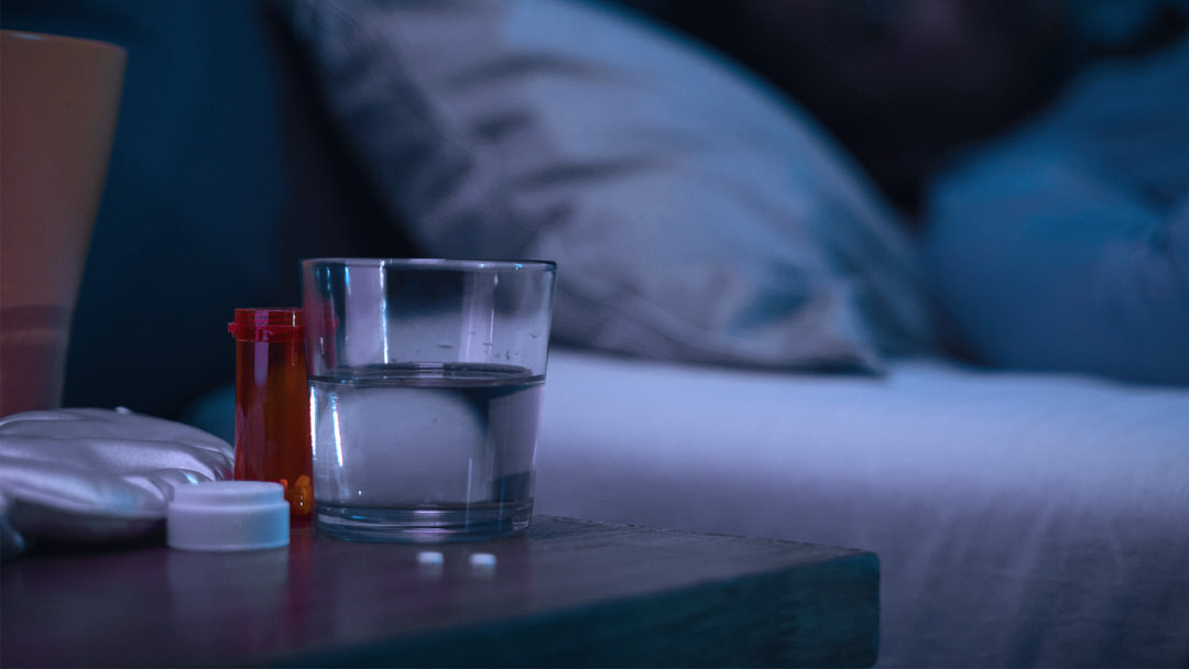 Glas Wasser und Medikamente auf einem Nachttisch bei gedämpftem Licht.