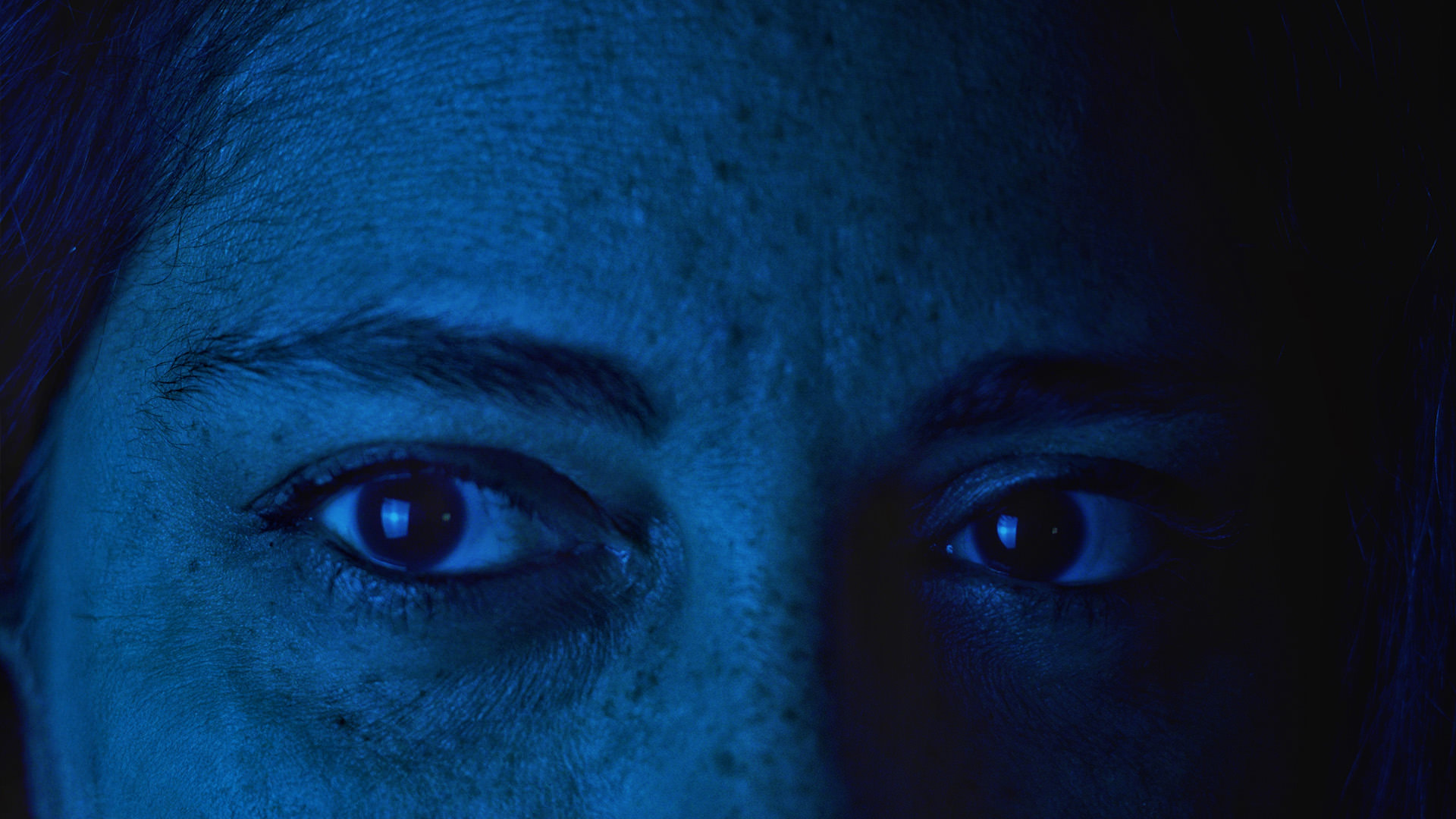 Nahaufnahme eines Gesichts im blauen Licht, Fokus auf die Augen.