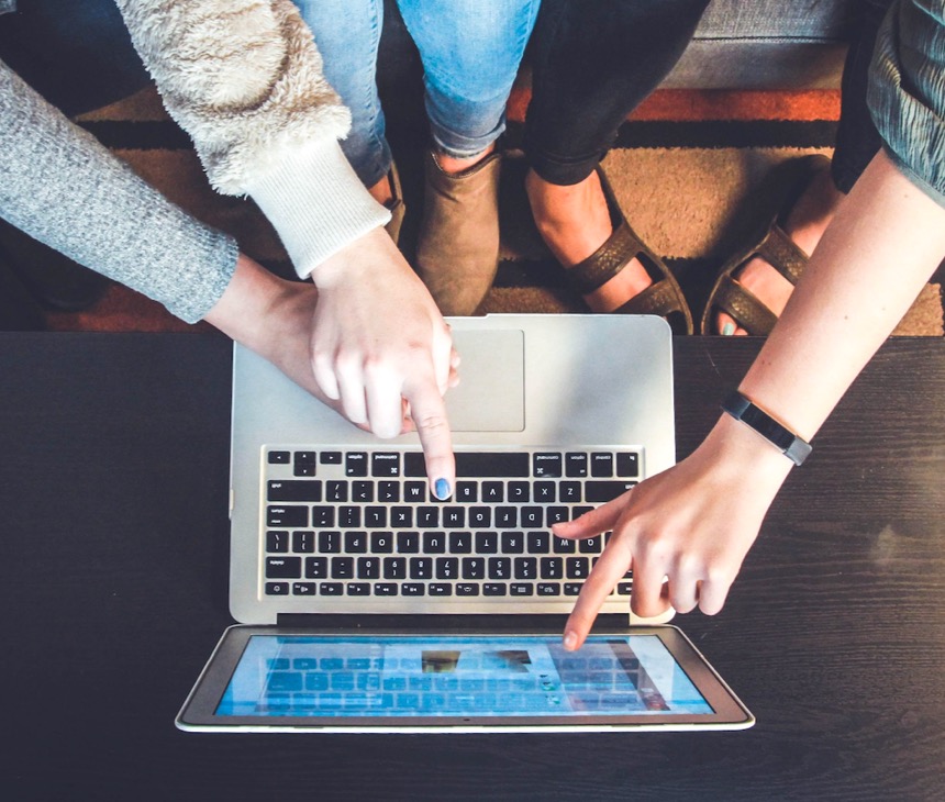 Fingers and hands pointing to a keyboard and laptop screen from above
