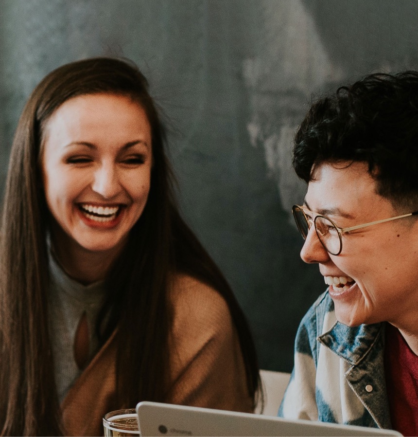 Two young women laughing sitting on a table