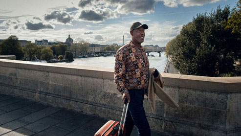 Allianz employee with a suitcase on hand, walking over a bridge in Paris with the Eiffel Tower in the background. 