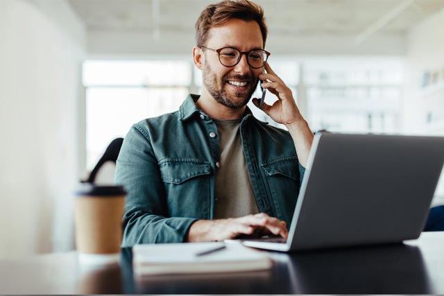 man in front of the laptop talking over the phone