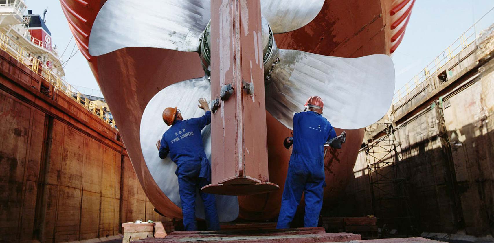 Two workers working on a large ship's propeller