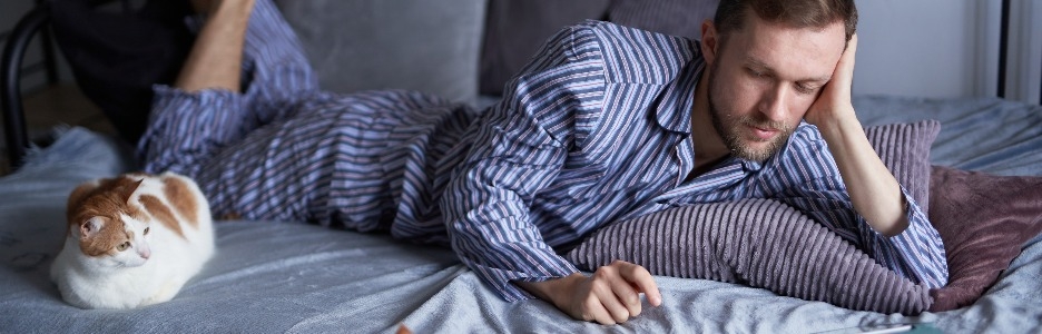 Imagen de un joven caucásico barbudo en pijama por la mañana acostado en una cama haciendo compras en línea o educando desde casa dos gatos atigrados sentados cerca imagen de alta calidad