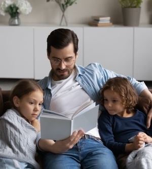 Imagen de un padre leyendo un libro a sus dos hijos en el salón de casa