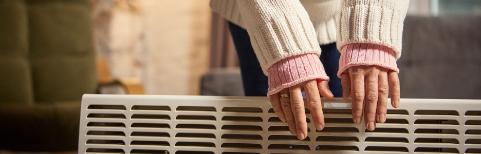 Imagen de una mujer de pie junto a un calefactor calentándose las manos en un acogedor apartamento moderno