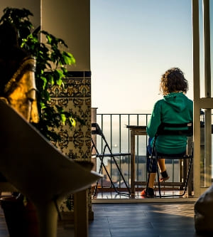 Imagen de vista trasera de una mujer con sudadera verde sentada en la terraza y leyendo o bebiendo café. Disfrutando de la soleada madrugada.