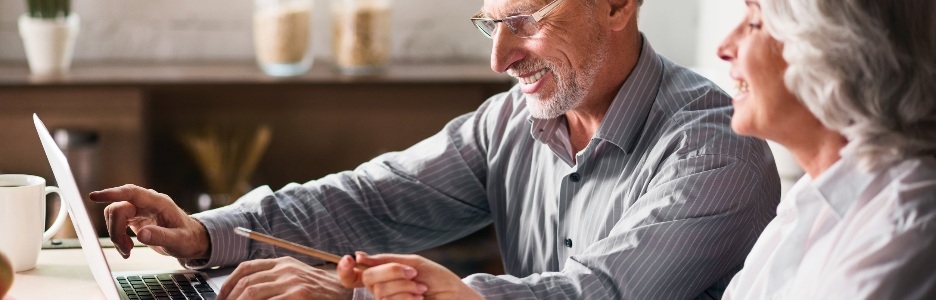 Imagen de una pareja de ancianos sentada en la cocina, usando la computadora y sonriendo