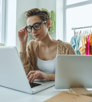 Imagen de una mujer joven segura que usa una computadora portátil mientras trabaja en la oficina de una tienda de moda