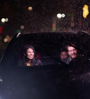 Imagen de un viaje nocturno, una familia feliz disfruta de momentos divertidos dentro de un automóvil mientras viajan a través de un clima lluvioso iluminado por el resplandor de los faros, risas y unión.