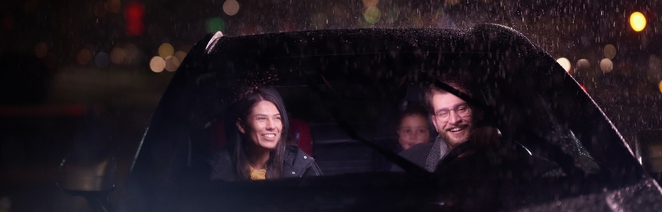 Imagen de un viaje nocturno, una familia feliz disfruta de momentos divertidos dentro de un automóvil mientras viajan a través de un clima lluvioso iluminado por el resplandor de los faros, risas y unión.