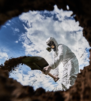 Imagen de vista desde el interior del pozo de un científico masculino irreconocible con máscara de gas usando equipo de pala para cavar suelo en la zona de peligro, analizando el entorno natural, ecologista profesional explorando la contaminación.
