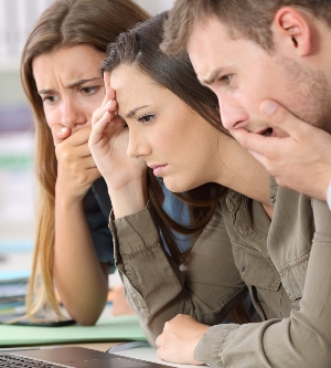 Imagen de tres adultos mirando una pantalla de forma preocupados