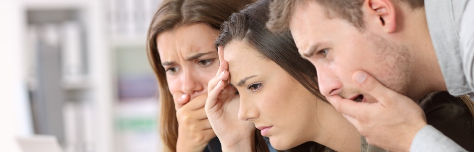 Imagen de tres adultos mirando una pantalla de forma preocupados