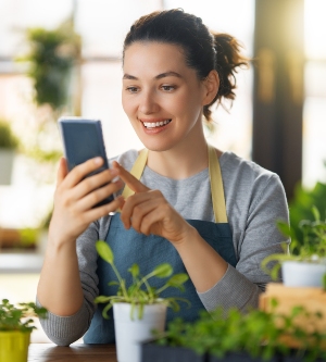 Imagen de una empresaria en su floristería navegando en su teléfono móvil