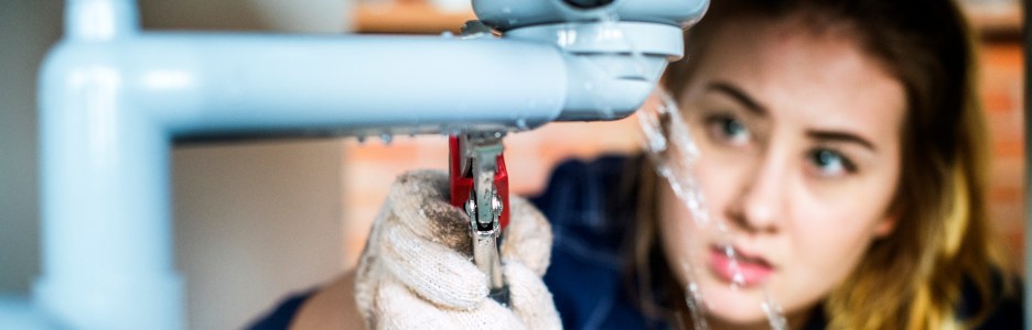 Imagen de un fontanero técnico con una llave para reparar un tubo de agua bajo el lavabo