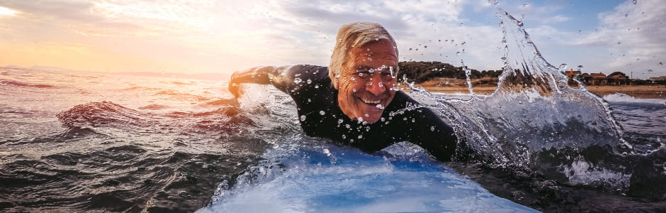 Imagen de un hombre de mayor edad surfeando en la playa