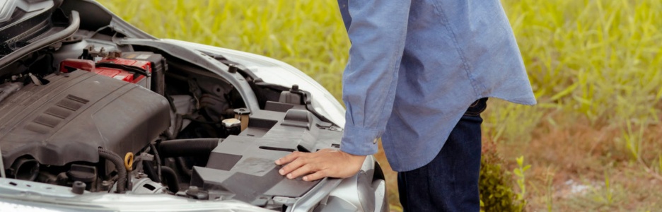 Imagen de un hombre solicitando asistencia para su coche mientras intenta resolver el problema en la carretera