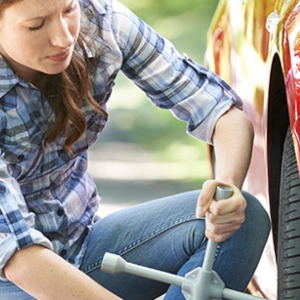 Imagen de una mujer cambiando las ruedas de su coche