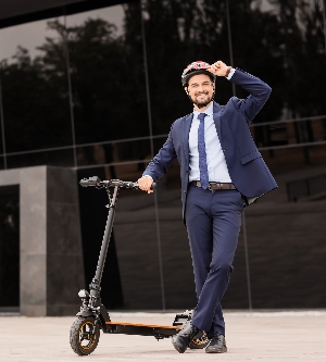 Imagen de un joven y apuesto empresario con casco en patinete eléctrico cerca de un edificio de oficinas