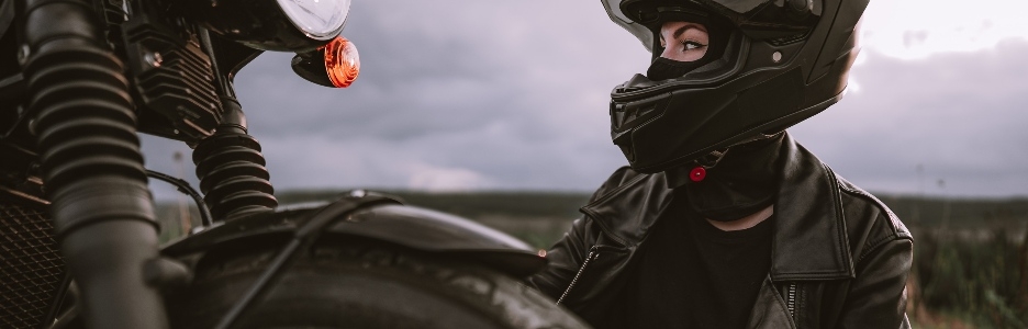 Imagen de mujer motociclista confiada en casco sentada cerca de la bicicleta. Motorista joven conductor al aire libre al atardecer.