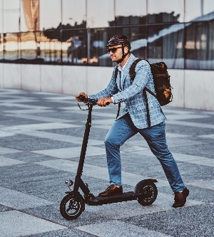 Imagen de un hombre moderno y alegre está conduciendo su scooter eléctrico cerca de su oficina después de un largo y duro día