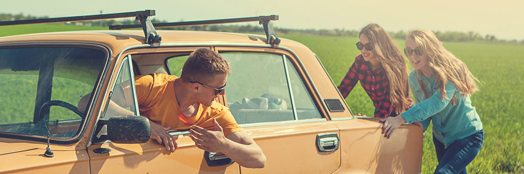 Imagen de dos chicas empujando un coche antiguo mientras el hombre lo intenta arrancar
