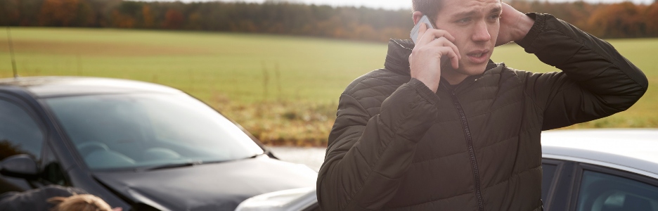 Imagen de un hombre hablando por el teléfono móvil después de sufrir un choque de coche en la carretera nacional