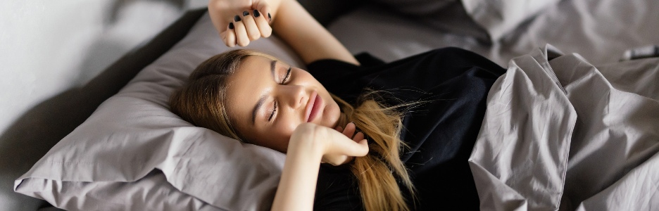 Imagen de una joven dama bonita y sonriente yace en la cama en el interior. Ojos cerrados.