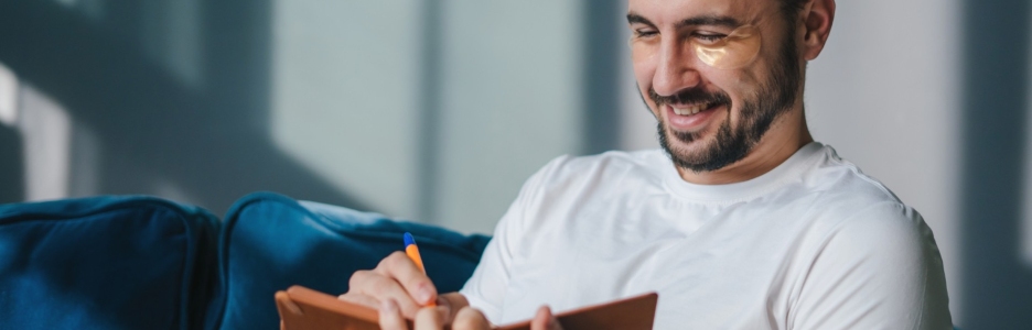 Foto de un hombre escribiendo en un libro con parches para ojeras