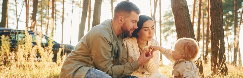 Imagen iluminada por la luz del sol, la feliz familia de padre, madre y pequeña hija está en el bosque