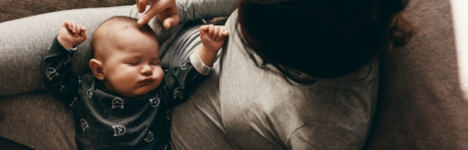 Imagen de una madre de reposo en el sofá con su bebé encima de ella